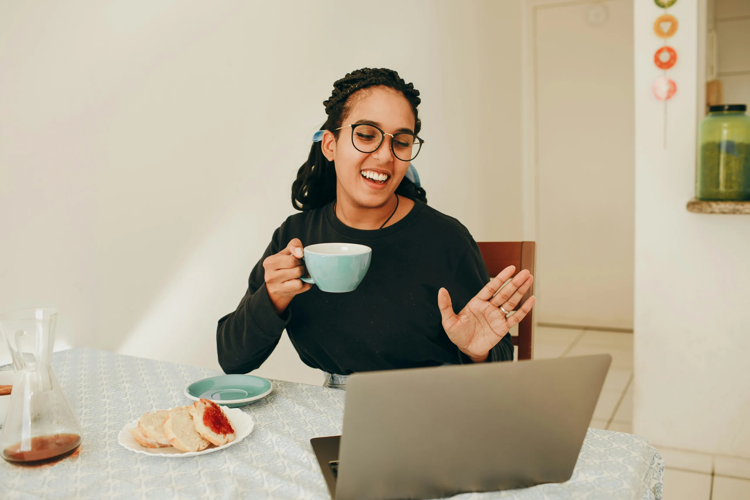 Meisje zwaait naar laptop scherm terwijl ze lacht met koffie in de hand